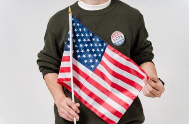 Flag held by a person with a "vote" pin | Photo by Sora Shimazaki