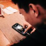 Man Touching Smartphone on Wooden Table | Photo by Luis Quintero