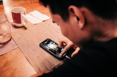 Man Touching Smartphone on Wooden Table | Photo by Luis Quintero