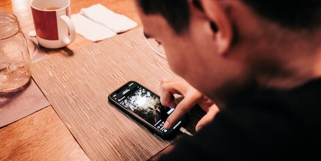 Man Touching Smartphone on Wooden Table | Photo by Luis Quintero